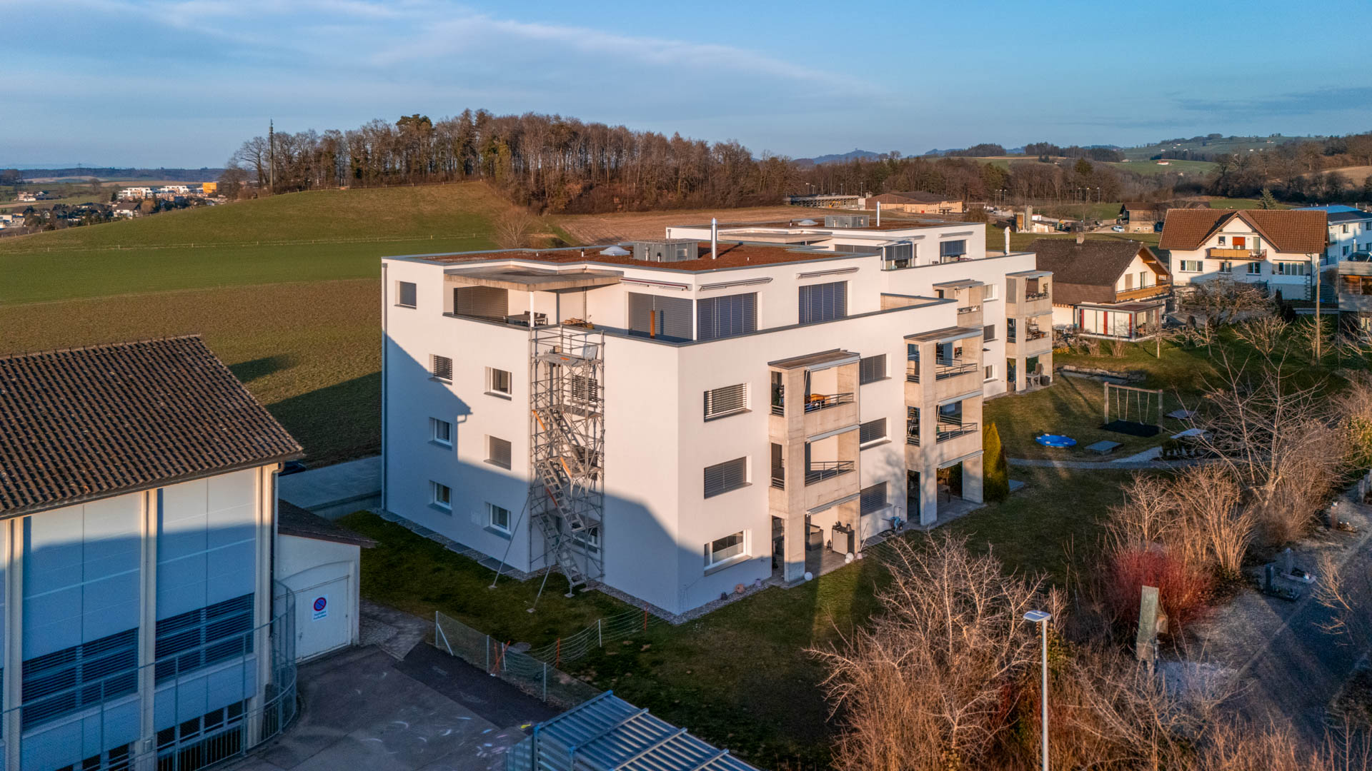 Treppenturm an einem neuen Mehrfamilienhaus, links eine Halle – Foto: KUGE Bau AG